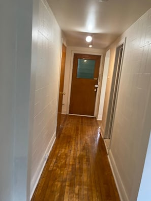 A narrow hallway with wooden flooring and white walls.