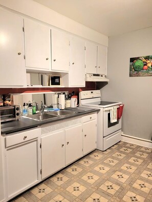 A kitchen with white cabinets, a stove, a microwave, and a sink.