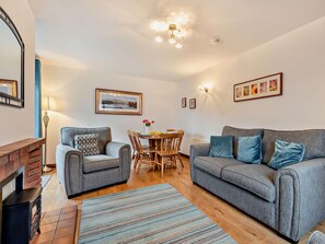 A living room with a fireplace, two sofas, a dining table with chairs, and a chandelier. - 3 Bed in Keswick (oc-93883) (Braithwaite)