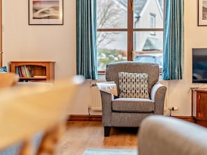A living room with a sofa, a small wooden side table, a radiator, a television, and a window with curtains. - 3 Bed in Keswick (oc-93883) (Braithwaite)