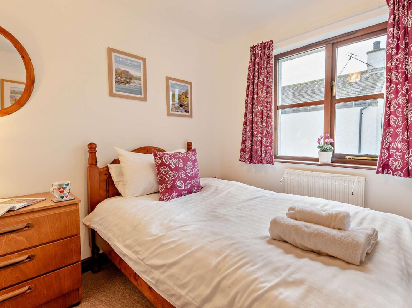 A bedroom with a wooden bed, white bedding, a bedside table with a cup, and a window with curtains.
