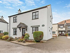 A two-story building with a white exterior, a small porch, and a sign reading 'ACORN COTTAGE.' - 3 Bed in Keswick (oc-93883) (Braithwaite)