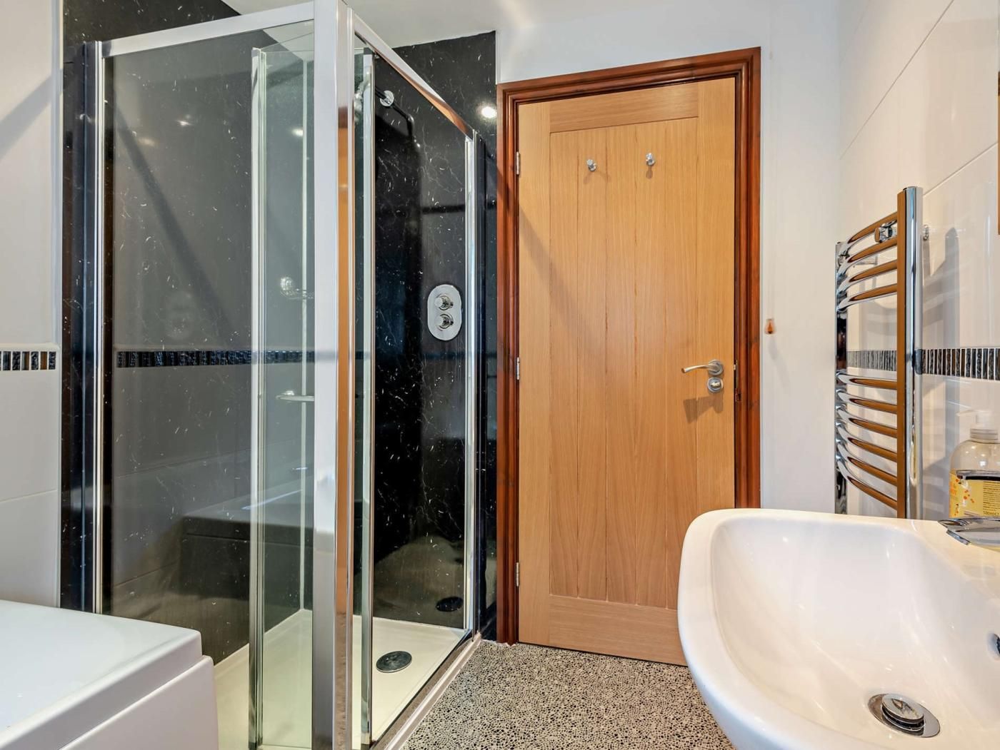 A bathroom with a glass shower enclosure, a wooden door, and a white sink.