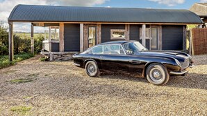 A vintage black car parked in front of a rustic building with a metal roof and wooden structure.