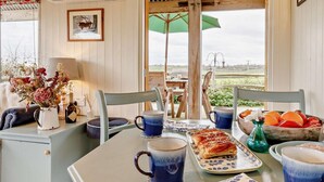 A dining area with a table set for two, featuring blue mugs, a plate with pastries, and a bowl of fruit.
