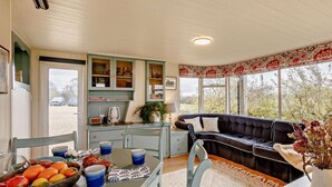 A cozy room with a dining table, chairs, a sofa, and a kitchen area with cabinets and a window.