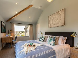 A bedroom with a bed, a desk, a chair, a window with a view, and a ceiling with exposed beams. - 5 Bed in Fowey (oc-93849) (Polruan)