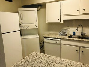 A compact kitchen with a refrigerator, a microwave, a dishwasher, and a granite countertop.