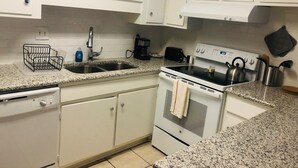Una cucina con mobili bianchi, un piano di lavoro in granito, un fornello, una lavastoviglie e una macchina da caffè.