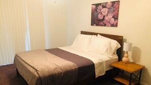 Un letto rifatto con una coperta marrone e bianca, un comodino in legno con una lampada e un quadro floreale al muro.