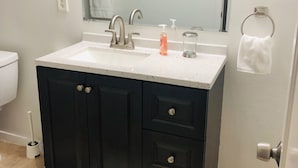 Un bagno con un lavandino bianco, mobili scuri, uno specchio, un porta asciugamani e un water.