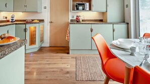 A compact kitchen with a microwave, a coffee maker, and a dining area with a table and chairs. - 2 Bed in Sandown (oc-93900) (Sandown)