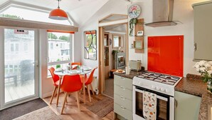 A modern kitchen with a gas stove, a dining table with chairs, and a view through the glass door. - 2 Bed in Sandown (oc-93900) (Sandown)