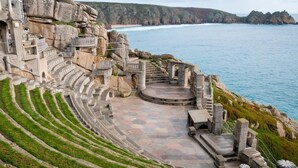 Ein Steine Amphitheater mit terrassenförmigen Sitzreihen und einer Bühne, das auf eine Küstenlandschaft blickt.