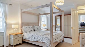 A four-poster bed with a floral bedspread, bedside tables with lamps, and a chandelier. - 1 Bed in Marazion (oc-53251) (Marazion)