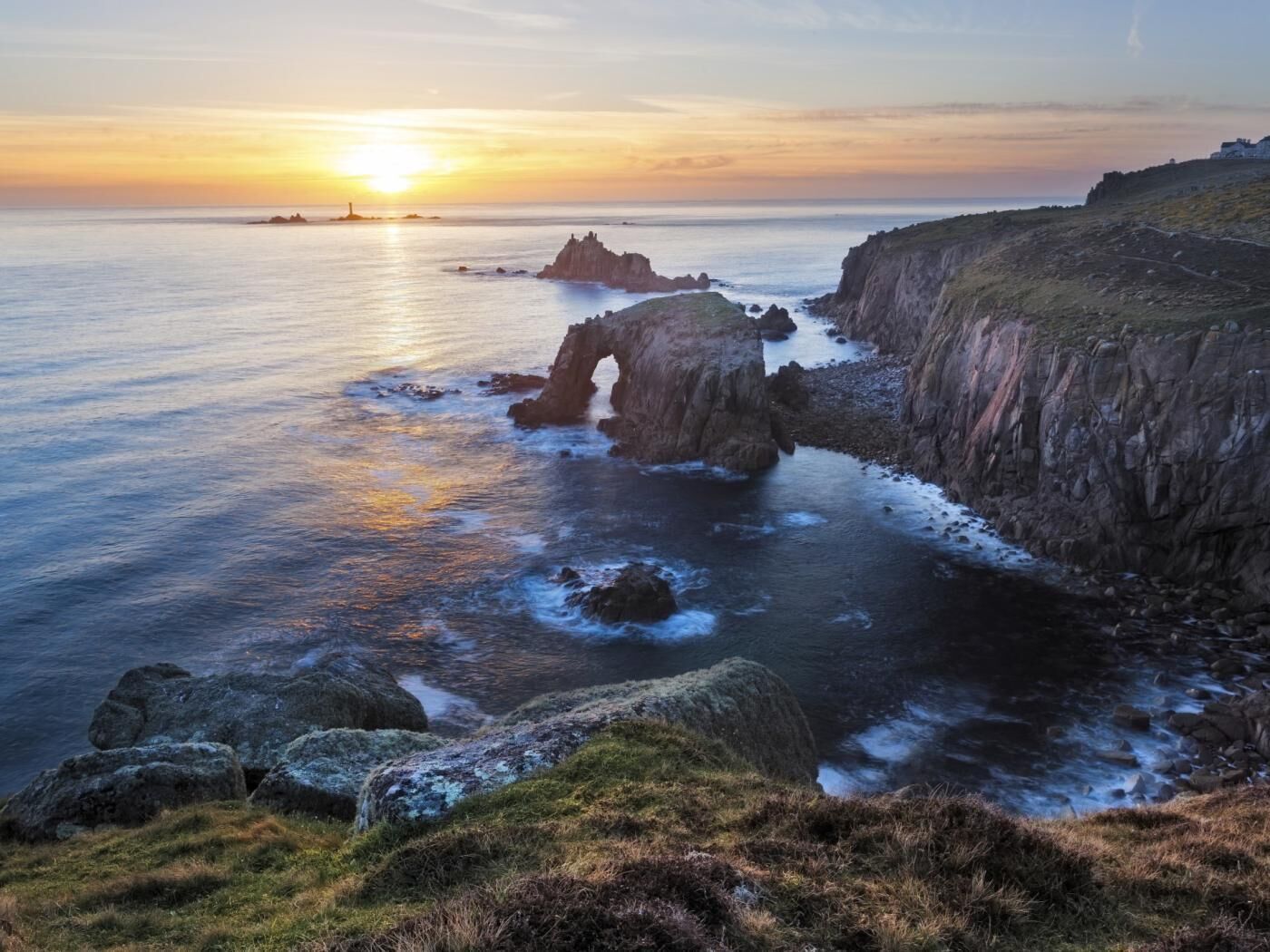 A coastal landscape with a prominent rock formation, a cliff, and a sunset over the sea.