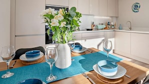 Une cuisine moderne avec des meubles blancs, une table à manger dressée avec de la vaisselle bleue et blanche, et un vase rempli de fleurs.