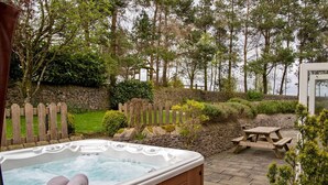 Een hottub in een tuin met stenen muren, een houten omheining en een picknicktafel.