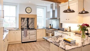 Een moderne keuken met witte kasten, een marmeren werkblad, een klok en hanglampen.