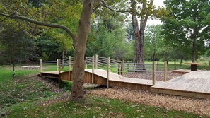 A wooden bridge over a dry riverbed, surrounded by trees and a grassy area. - Eagle Creek Lodge (Worth Township)