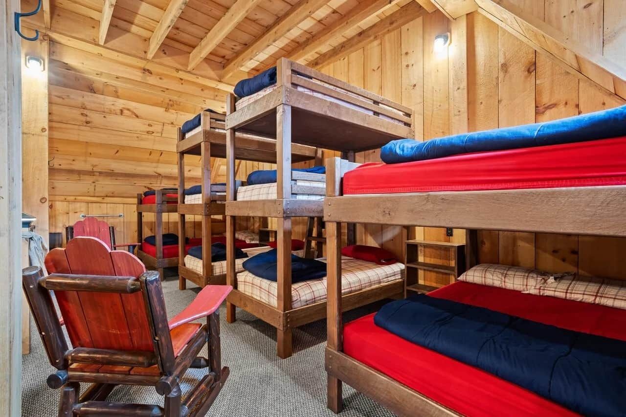 Etagenbetten mit roter und blauer Bettwäsche, Holzwände und ein hölzerner Schaukelstuhl.