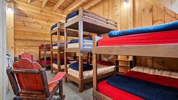 Letti a castello con biancheria rossa e blu, pareti in legno e una sedia a dondolo di legno.