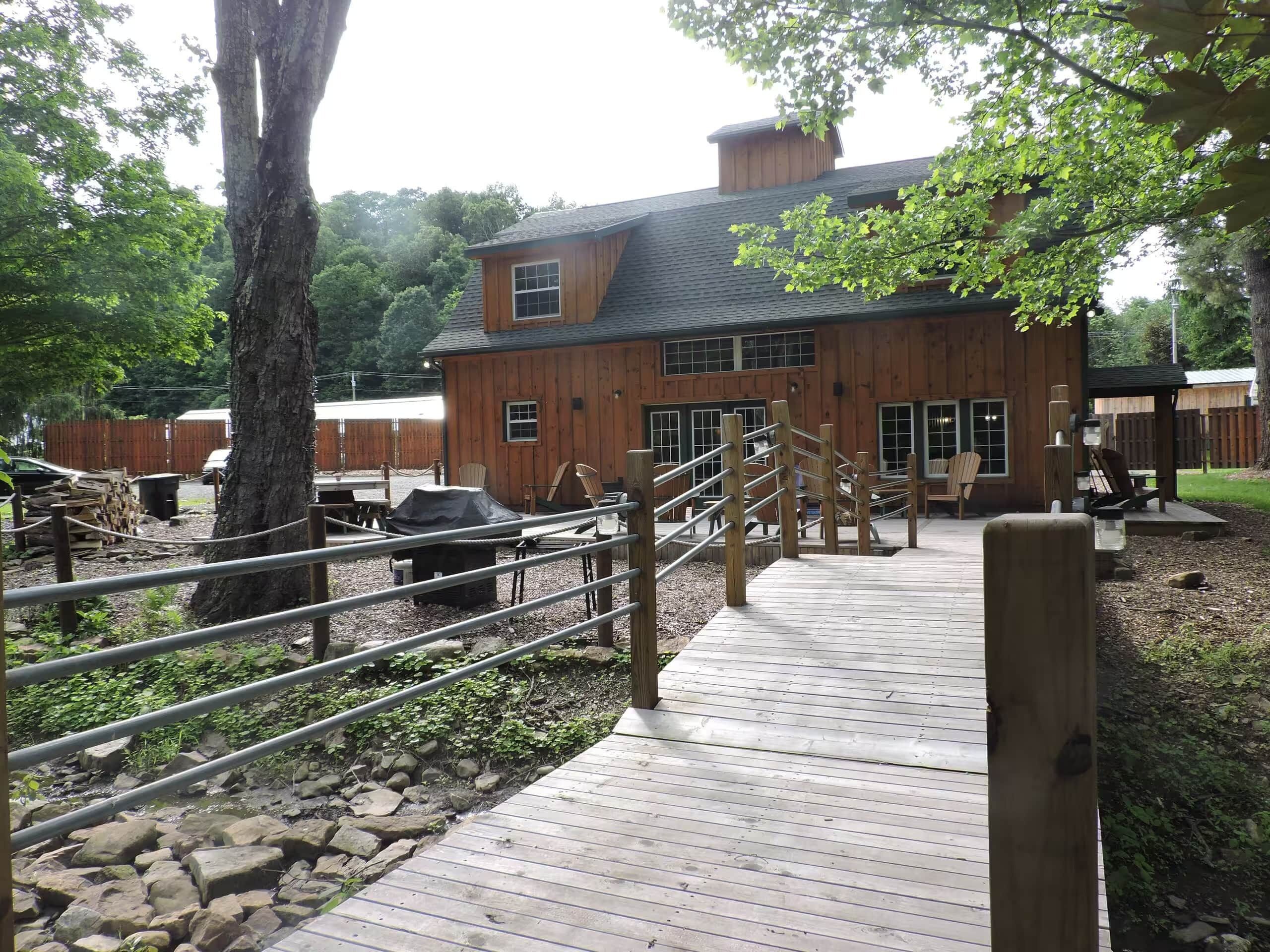 A wooden building with a covered deck, outdoor seating, and a fenced area with chairs.