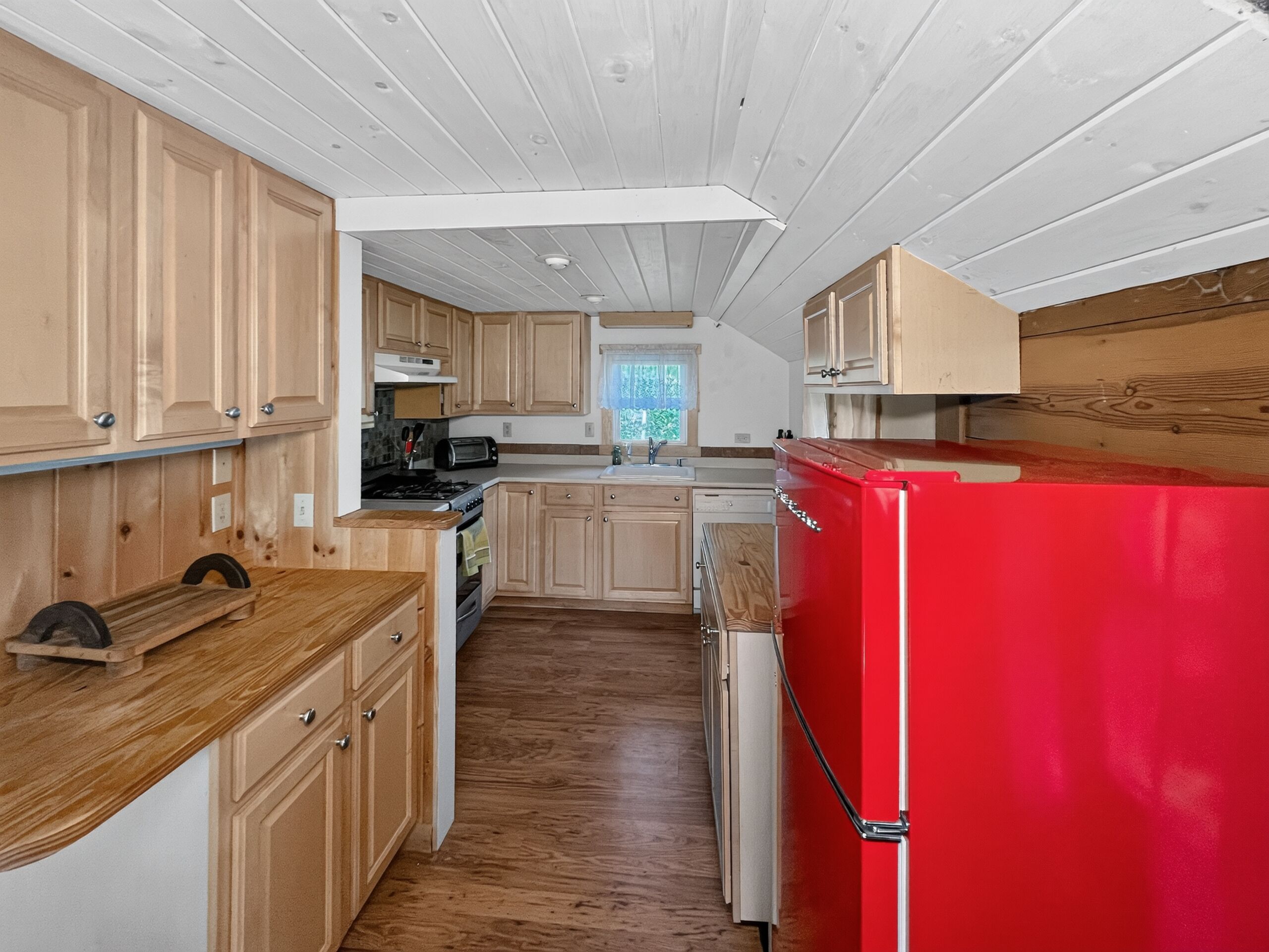 Une cuisine compacte avec des meubles en bois, un réfrigérateur rouge, une cuisinière et une fenêtre donnant sur un beau paysage.