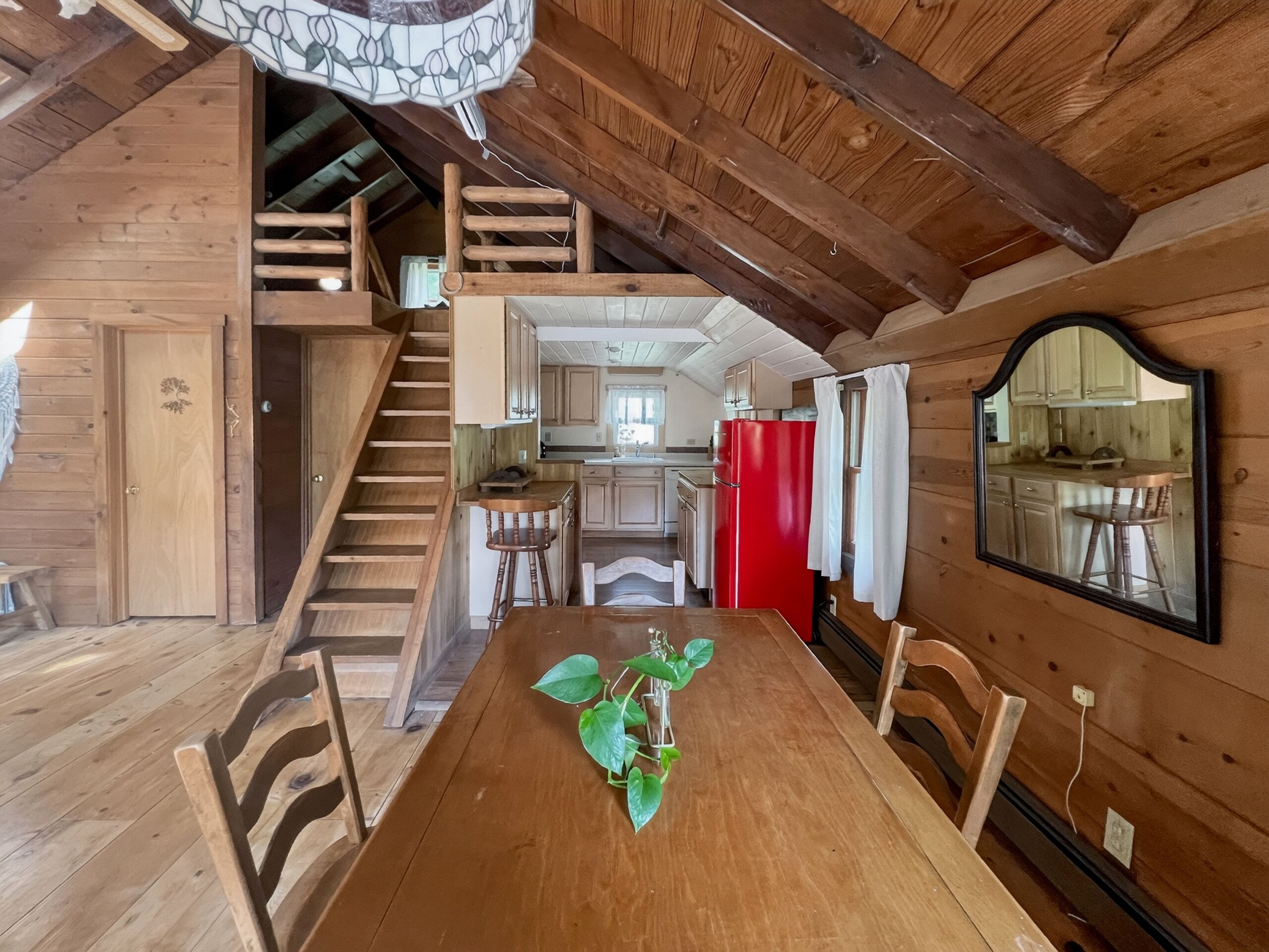 Un intérieur en bois comprenant une table à manger, des chaises, un escalier et un coin cuisine.