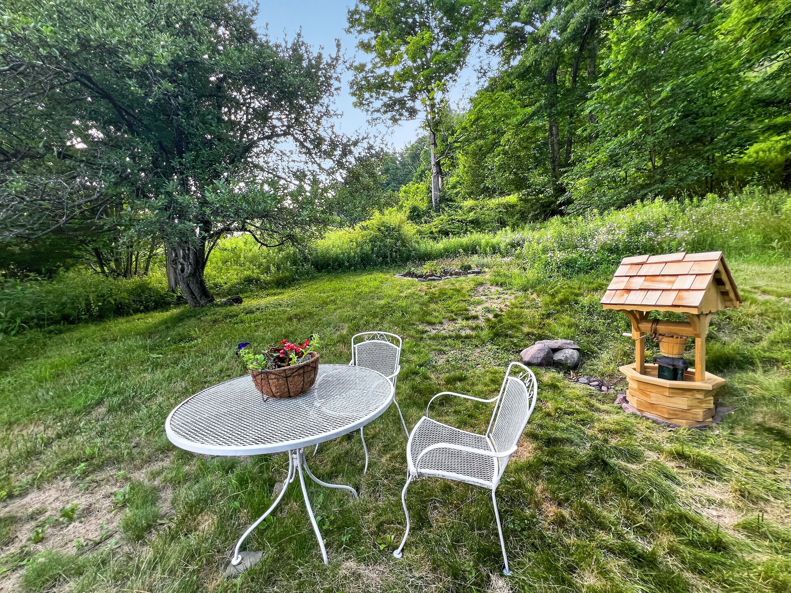 Une table ronde en métal, accompagnée de deux chaises, d’une nichoir en bois et d’une plante en pot.