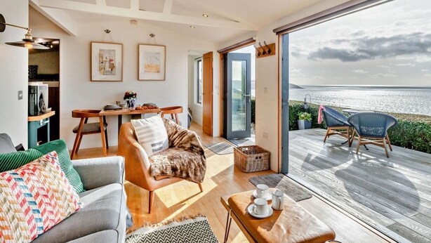 Ein modernes Wohnzimmer mit Meerblick, einer Holzterrasse und einem Essbereich.