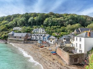 A coastal town with buildings along the beach, a stone wall, and a forested hill in the background. - 1 Bed in Torpoint (oc-93517) (Tregonhawke)