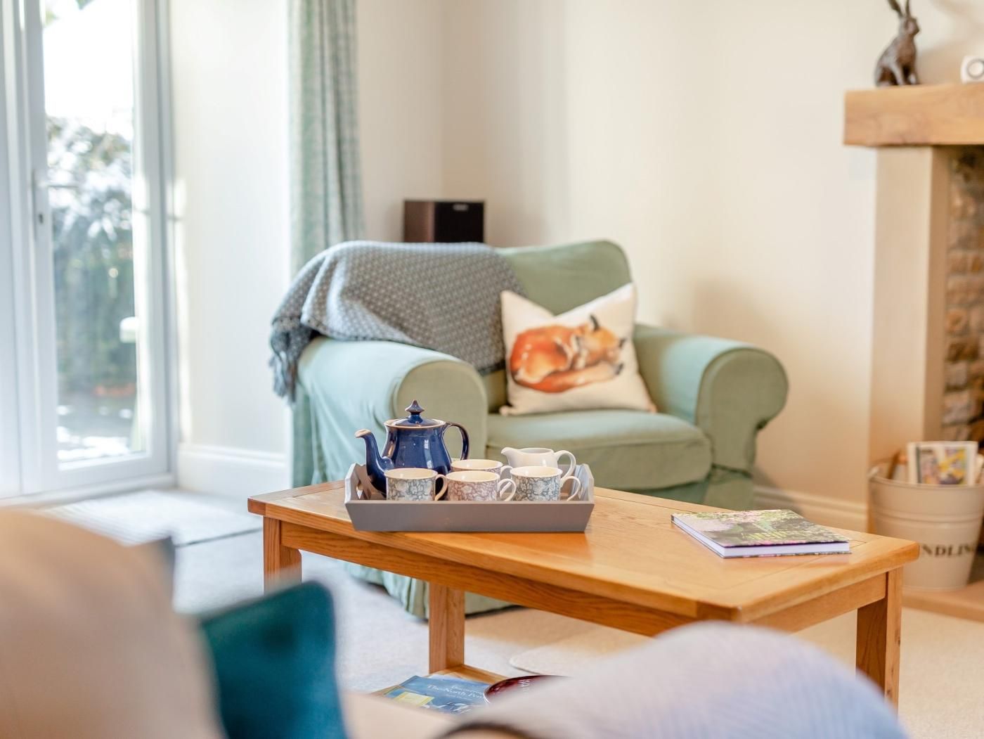 Een knusse woonkamer met een bank, een tafel met theepot en kopjes, en een open haard.