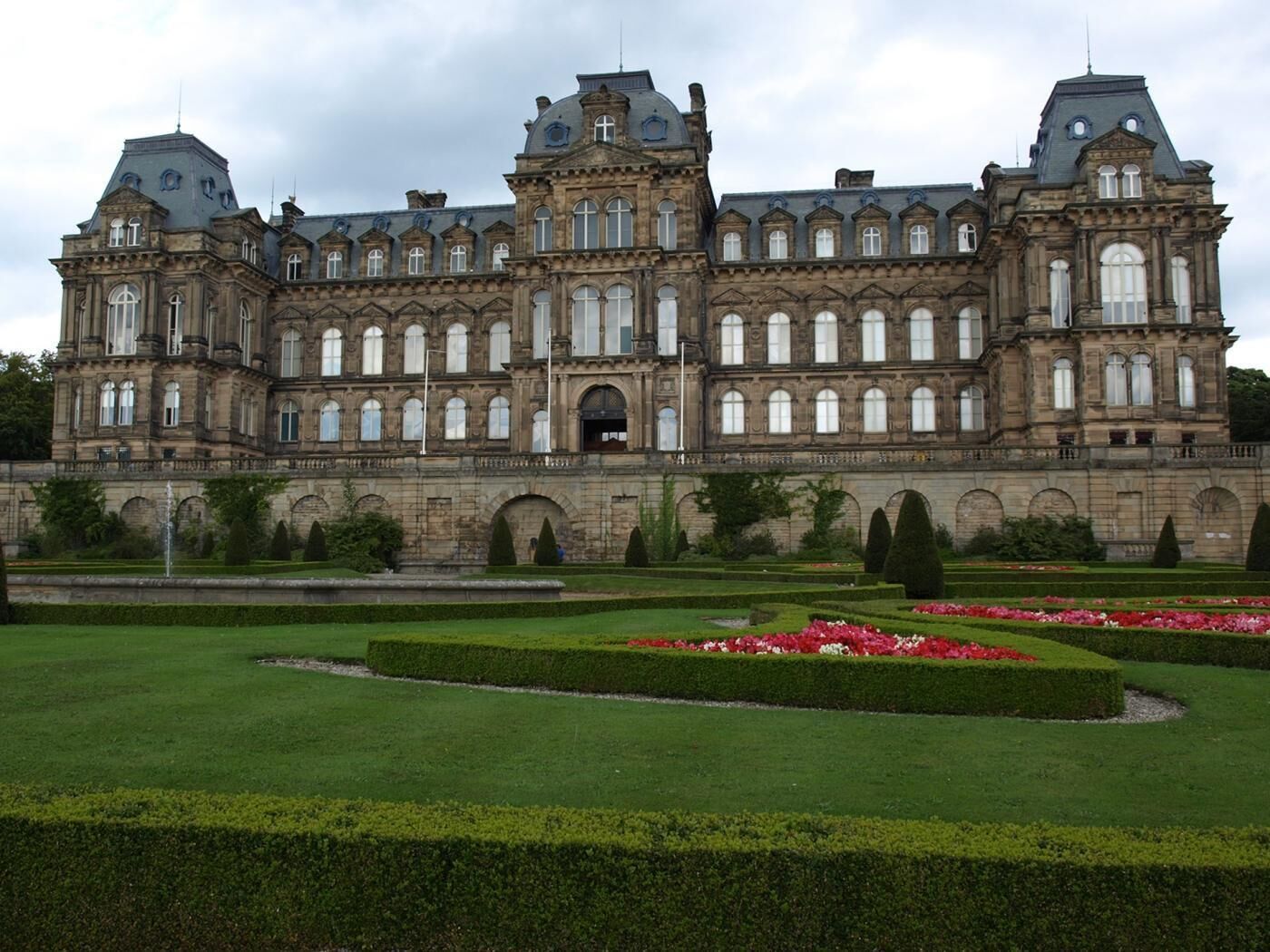 Ein großes, historisches Gebäude mit symmetrischer Architektur, zahlreichen Fenstern und einem formalen Garten mit Hecken und Blumenbeeten.