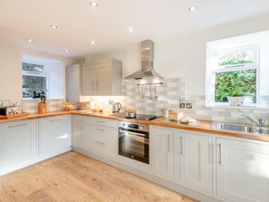 A modern kitchen with white cabinets, a stainless steel range hood, a built-in oven, and a window with a view of greenery.