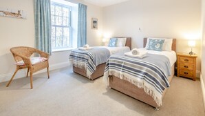 A bedroom with two beds, a chair, a window with curtains, and a nightstand. - 3 Bed in Barnard Castle (oc-93880) (Middleton-in-Teesdale)
