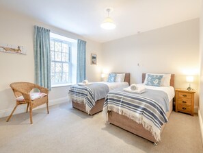 A bedroom with two beds, a chair, a window with curtains, and a nightstand.