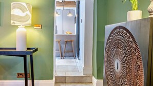 Un corridoio con una lampada da tavolo, un elemento decorativo a parete e una scala che conduce a una zona cucina.