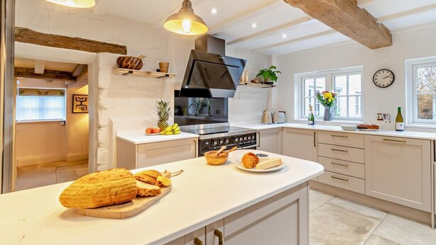 Una cucina moderna con un'isola centrale, travi in legno e illuminazione a sospensione.