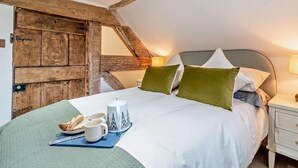 Una camera da letto con soffitto spiovente, una porta in legno, un letto con cuscini, un comodino con una lampada e un vassoio con prodotti per la colazione.