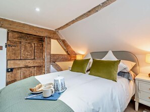 Ein Schlafzimmer mit schrägen Wänden, einer Holztür, einem Bett mit Kissen, einem Nachttisch mit Lampe und einem Tablett mit Frühstücksangeboten.