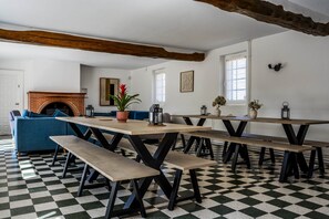 A room with a checkered floor, a fireplace, a blue sofa, and a long table with benches.