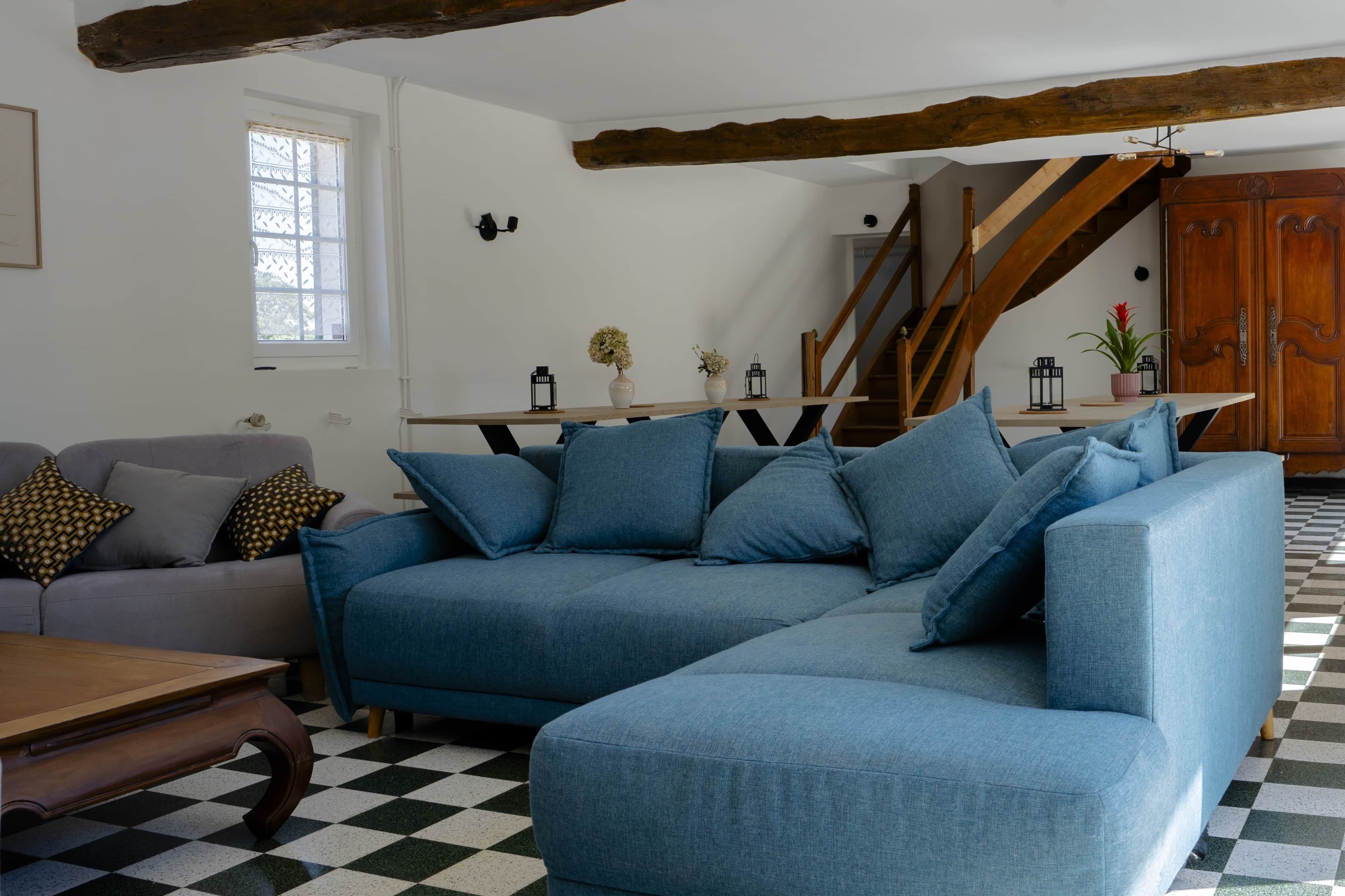 Ein Wohnzimmer mit Schachbrettmuster-Boden, einem blauen Sofa, einem Holztisch und einer Treppe.