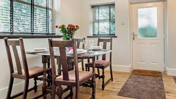 A dining area with a wooden table and chairs, a vase with flowers, and a view of the outside through the windows.