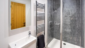 Ein modernes Badezimmer mit einem weißen Waschbecken, einer Holztür, einer Duschkabine aus Glas und einem Handtuchhalter.