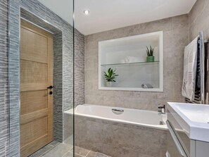 A modern bathroom with a glass shower enclosure, a wooden door, a large bathtub, and a glass shelf with a plant. - 1 Bed in Woolacombe (oc-93920) (Woolacombe)