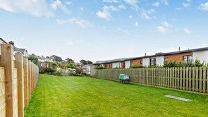 A residential area with a well-maintained lawn, a wooden fence, and a row of houses with modern architecture. - 1 Bed in Woolacombe (oc-93920) (Woolacombe)