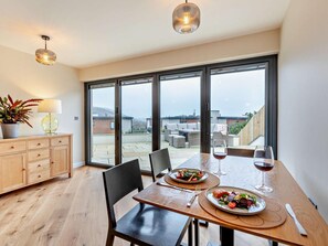 A dining area with a table set for two, a potted plant, and a view of the outdoor patio. - 1 Bed in Woolacombe (oc-93920) (Woolacombe)