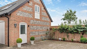 A brick house with a sloped roof, a white door, and a small garden with potted plants. - 1 Bed in Blandford Forum (oc-93922) (Spetisbury)