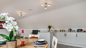 A modern kitchen with white cabinets, a dining table with chairs, and a ceiling light fixture. - 1 Bed in Blandford Forum (oc-93922) (Spetisbury)